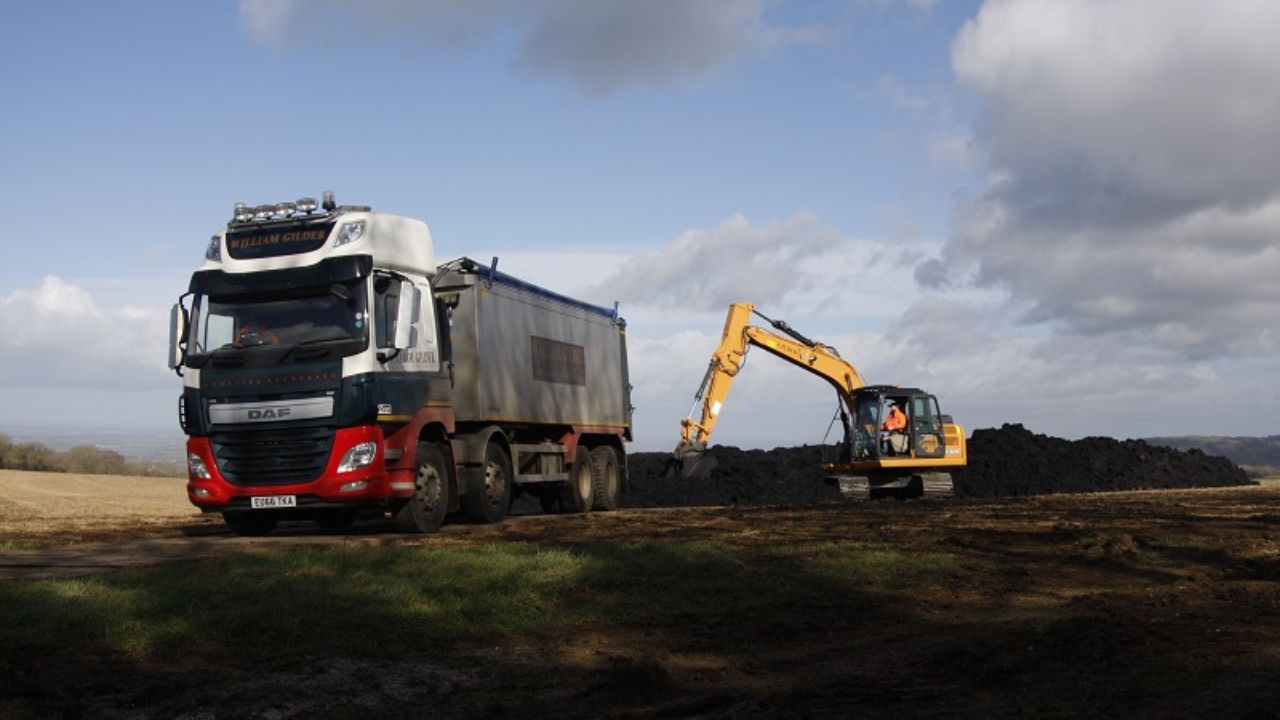 A digger behind a lorry harvesting a field